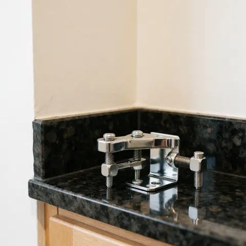 Stainless steel clamp with screws resting on a polished black granite countertop against warm cream walls
