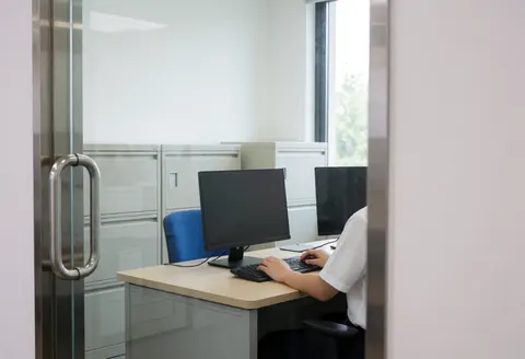 Administrator working at a desk with a computer, file cabinets, and a window in a clean professional chess school office.