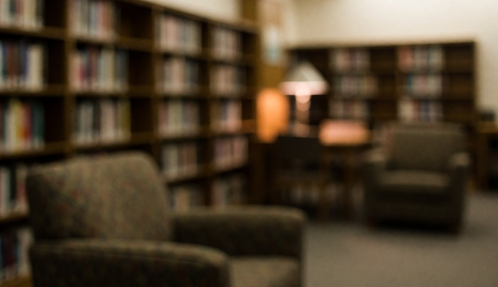 Soft focus background of library bookshelves and upholstered armchairs with warm lighting, suitable for educational text overlays.