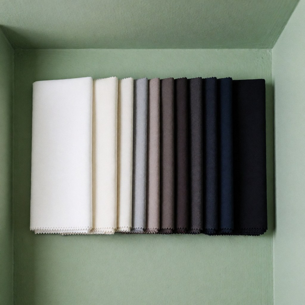 White to black gradient sewing fabric samples arranged on a soft green wall, ideal for tailor shop displays