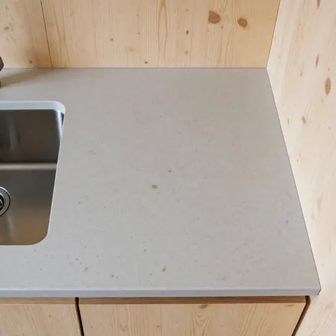 Top view of a gray quartz countertop with an integrated stainless steel sink, light wood walls, modern and functional kitchen design