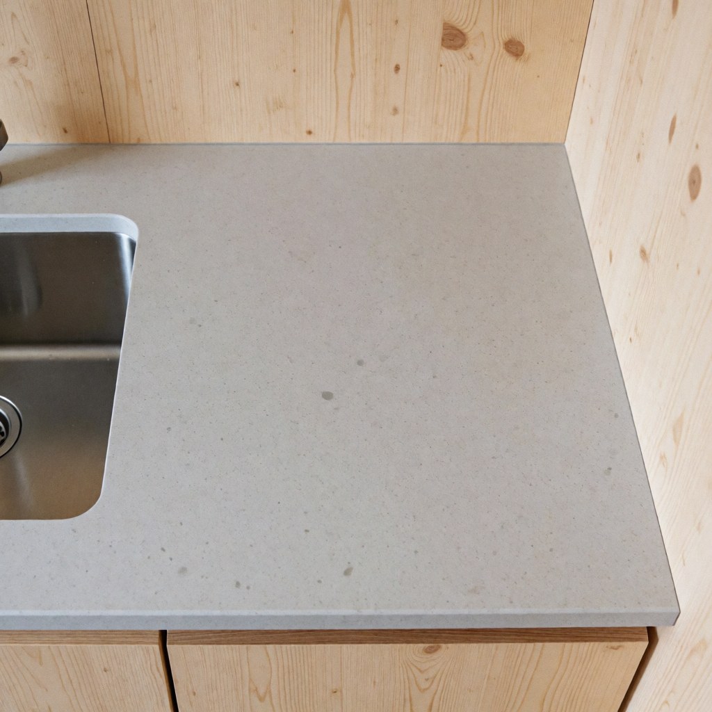 Top view of a gray quartz countertop with an integrated stainless steel sink, light wood walls, modern and functional kitchen design