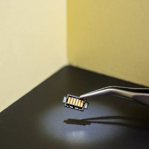 A replacement USB-C connector with gold contacts held by metal tweezers on a dark surface for phone repair