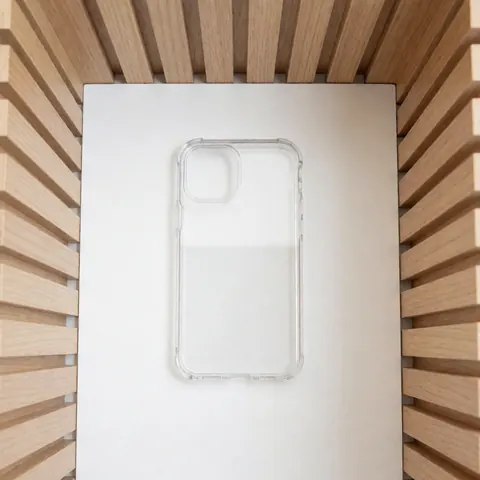 Clear protective phone case with precise cutouts placed on a white surface surrounded by light wood walls under soft lighting
