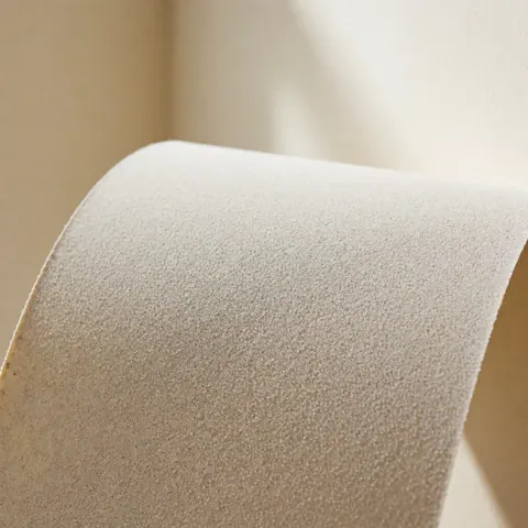 Close-up of fine-grit sandpaper sheet with visible texture and curved edge resting on a soft beige wall surface