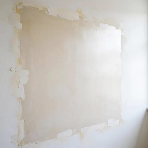 A repaired wall with smooth texture and adhesive tape along the edges, prepared for painting under bright and even lighting.