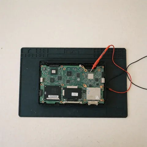 Computer motherboard on anti-static mat with multimeter for technical diagnosis, even lighting, white background
