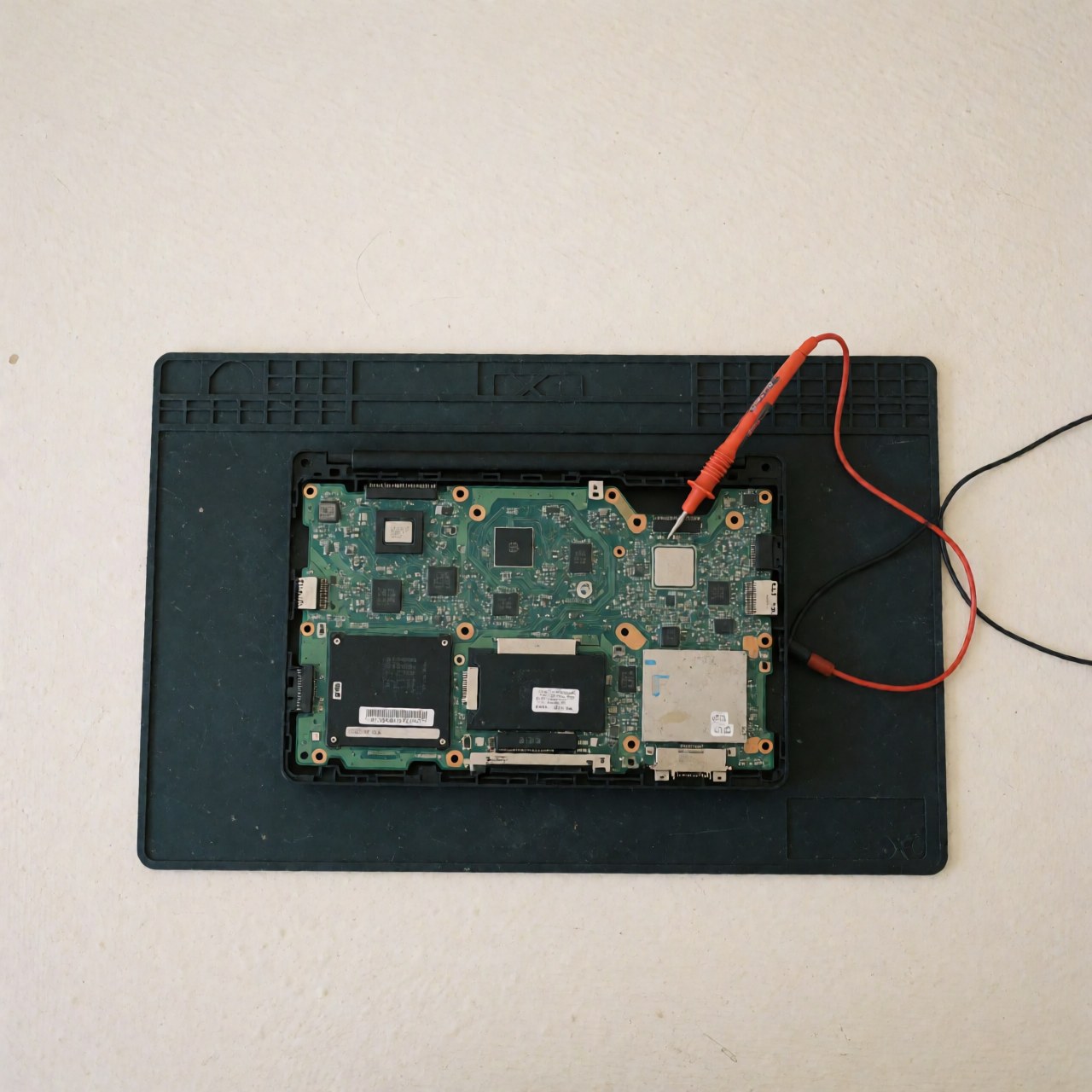 Computer motherboard on anti-static mat with multimeter for technical diagnosis, even lighting, white background