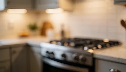 Blurred gas stove with neutral cabinets and countertop, warm lighting, suitable for text overlay.