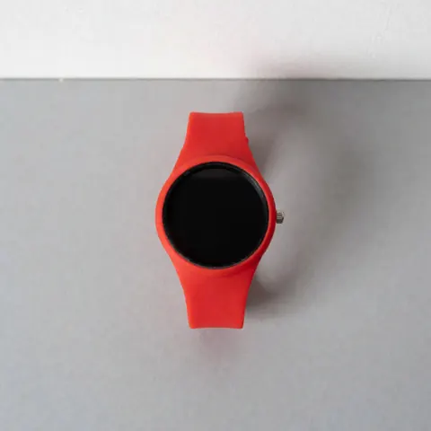 Top view of a red sports watch with a black dial and silicone strap on a neutral gray surface