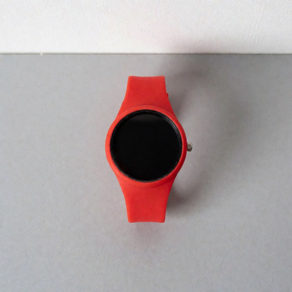 Top view of a red sports watch with a black dial and silicone strap on a neutral gray surface