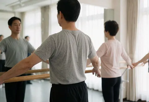 An adult man stretches at a ballet barre in a dance studio with natural light and mirrors.