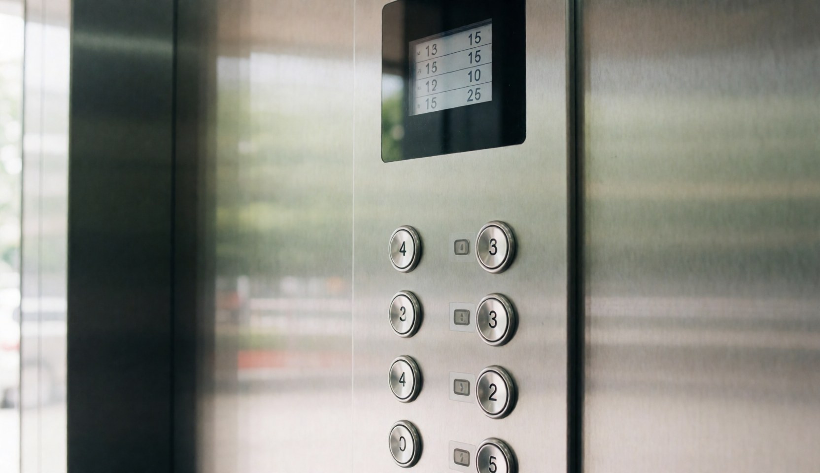 Close-up of a modern elevator control panel featuring circular metallic buttons and a digital floor display against a blurred background.