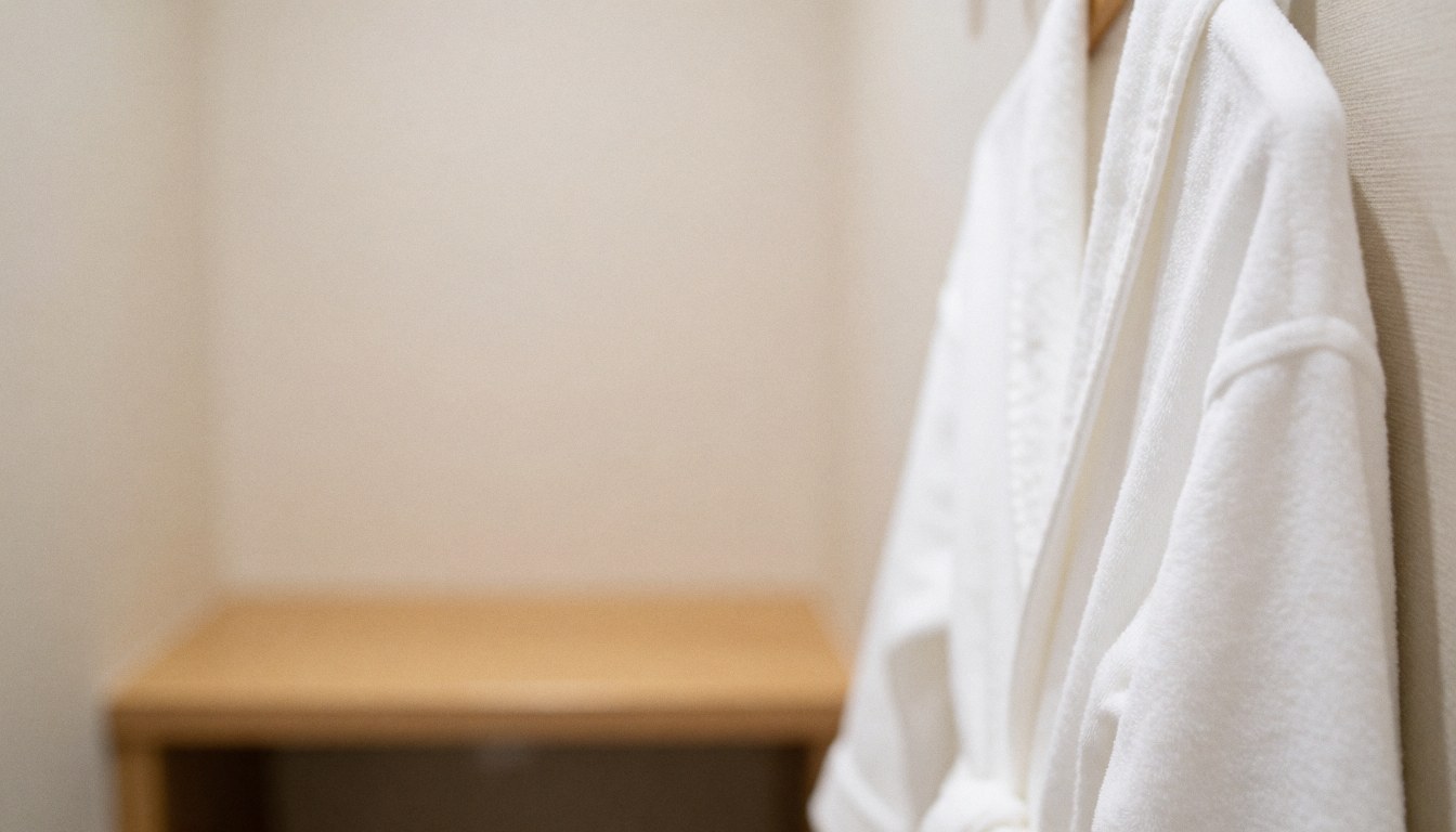 White spa robes hanging on a wooden rack with a blurred background, creating a calm and neutral atmosphere for text overlays.