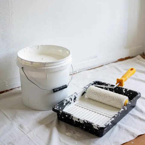 White paint bucket and roller in a tray on white cloth ready for painting walls