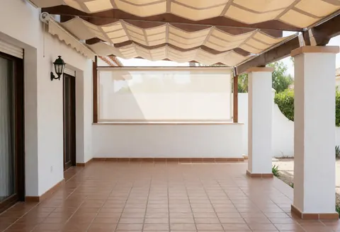 Wooden and beige fabric awning shading a tiled patio with white walls and natural light