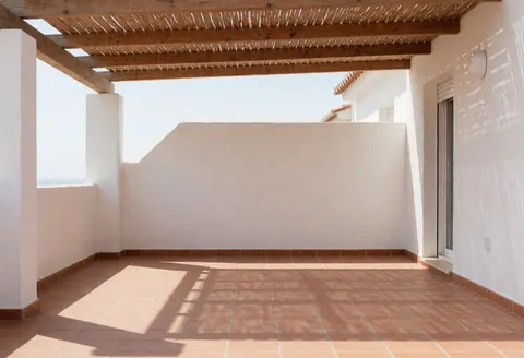 Residential patio featuring a wooden awning with geometric shadows on terracotta tile floor and stucco walls, showcasing awning installation.