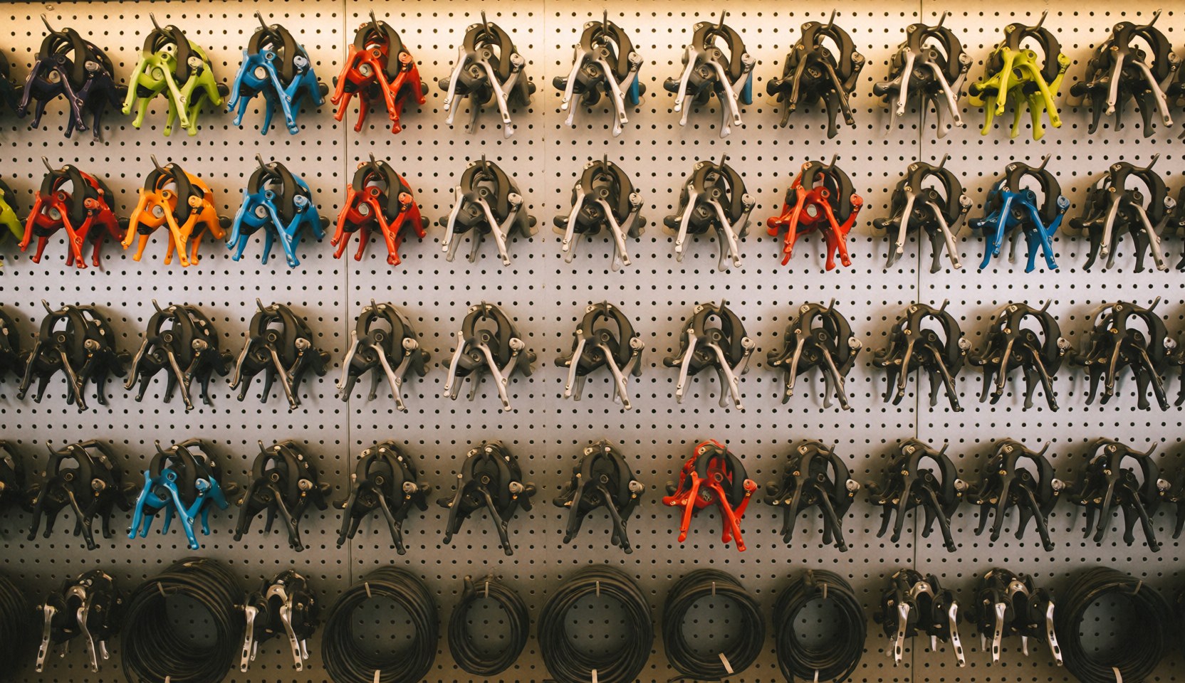 Rows of bicycle components and tools organized on a textured metal wall, providing a clean background for text overlay in a bike repair shop setting.