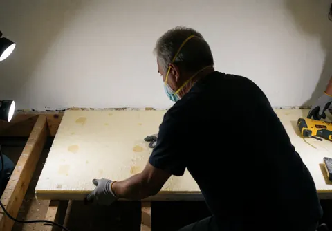 Worker installing thermal insulation panels on a residential roof with visible tools, wood, and work lights