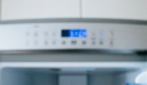 Close-up of a refrigerator control panel illuminated by soft blue light, serving as a clean professional background for text overlay.