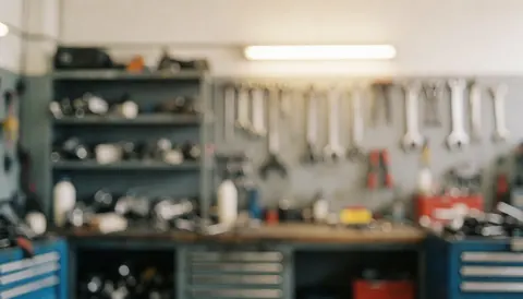 Hanging tools, parts shelves, and toolboxes in an engine repair workshop with warm lighting and a blurred background ideal for text.