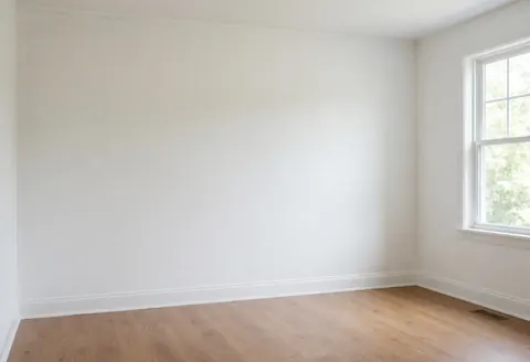 Empty room with freshly painted white walls, light wood flooring, and natural light from a window, ideal for showcasing interior painting services.