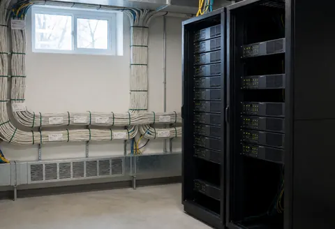 Server room with black racks, labeled white cables, and small windows. Ideal for security camera installation.
