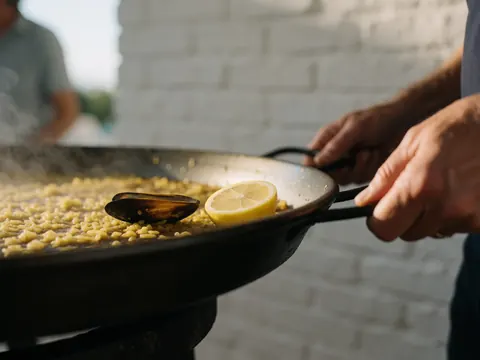 Close-up of grilled paella with mussels and lemon served on a grill at a resort with a white brick wall background.