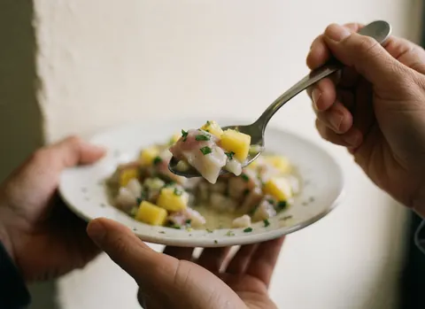 Fresh ceviche with fish, mango, and cilantro on a spoon held by hands over a white plate