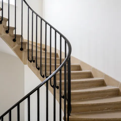 Curved black iron railing on beige stone steps with white walls, viewed from above, suitable for staircase installers