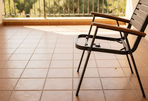 Metal garden chair with wooden seat on a tiled patio with natural light and railing in the background