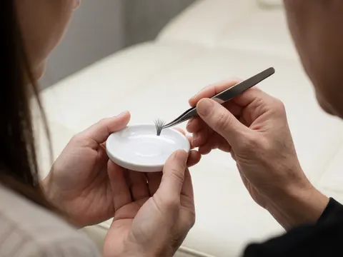 Professional tweezers hold false eyelashes on a white palette in a beauty salon with a blurred background