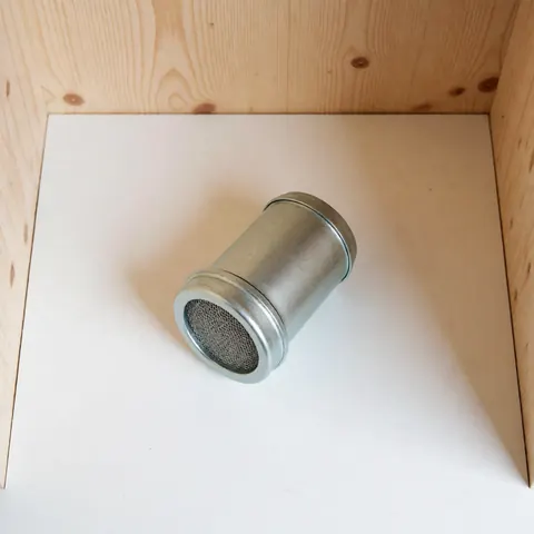 Top view of a cylindrical metal gas filter with mesh, placed in a wooden box on a white surface, suitable for gas installation products.
