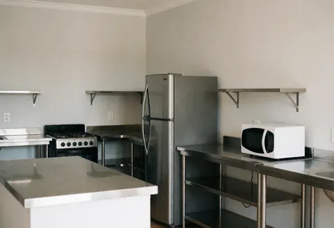 Shared hostel kitchen featuring a refrigerator, microwave, stove, and clean stainless steel countertops.
