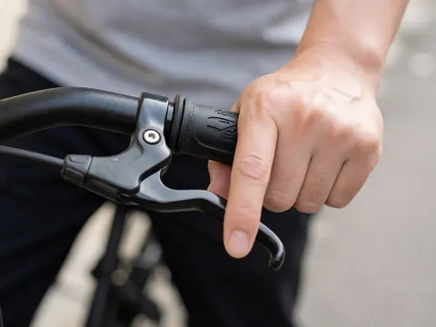 Close-up of an adult hand gripping a bicycle handlebar with brake, showing grip detail against a blurred wall and pavement background
