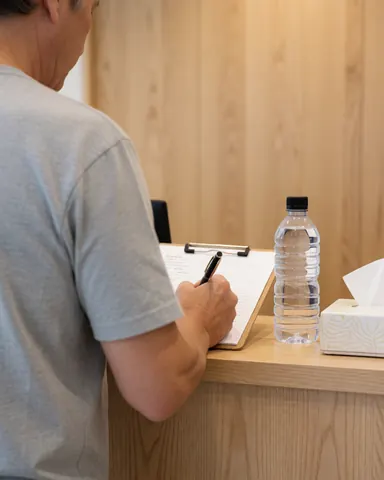 A client signs paperwork at a sports massage clinic reception desk with water and tissues nearby