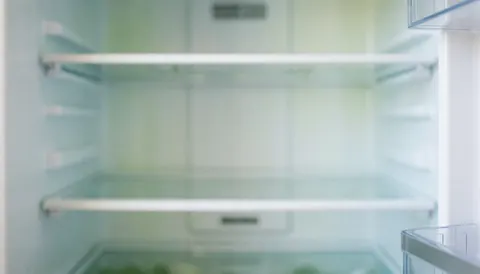 Clean white refrigerator interior with empty shelves and soft lighting, providing a neutral background for commercial text overlays.