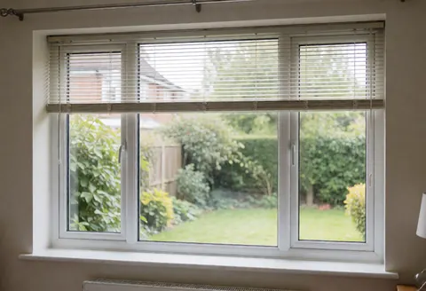 White insulated window with lowered blinds, green garden view, natural light, clean and orderly interior
