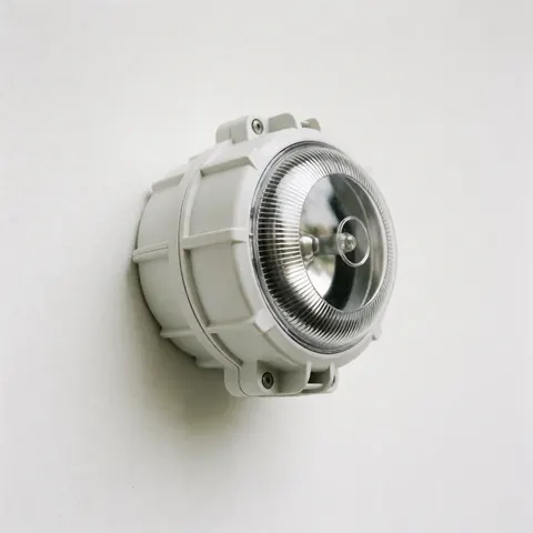 White industrial-grade outdoor alarm siren mounted on a white wall with a clear protective lens.