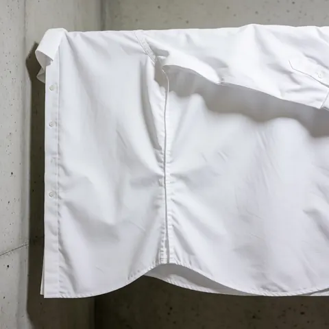 White formal shirt with a clean repaired side seam hanging against a concrete wall under bright, even lighting.