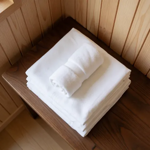 Clean folded white towels on a dark wooden table with light wood panel walls and soft natural lighting