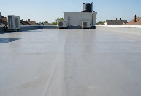 Gray concrete flat roof prepared for waterproofing with air conditioning units and water tank in background under clear blue sky
