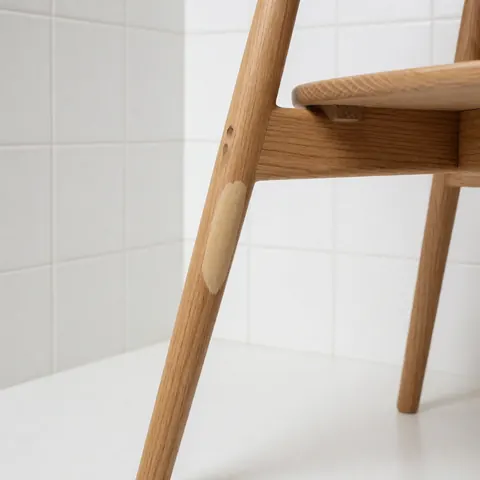 Close-up of a repaired light wood chair leg showing visible restoration work against a white tiled background.