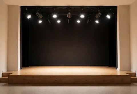 An empty dance studio stage featuring professional spotlights, beige walls, and a wooden floor, ready for professional dance classes.
