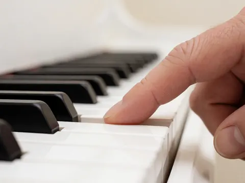 Macro shot of an adult finger pressing a white piano key with a blurred background and soft lighting, focusing on touch and precision.