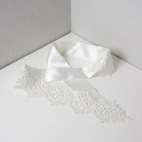 White lace sash placed on the corner of a white table with light gray walls and soft professional lighting