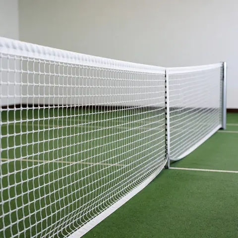 Centered white tennis net with silver posts on a green court against a white wall under bright professional lighting