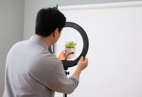 Photographer adjusting ring light around a succulent plant in a white studio for macro product photography.