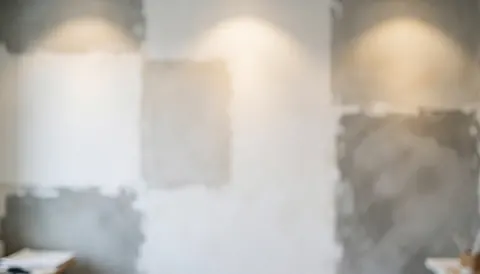 Out of focus wall featuring white and gray plaster samples with warm lighting, providing a neutral backdrop suitable for business text overlays.