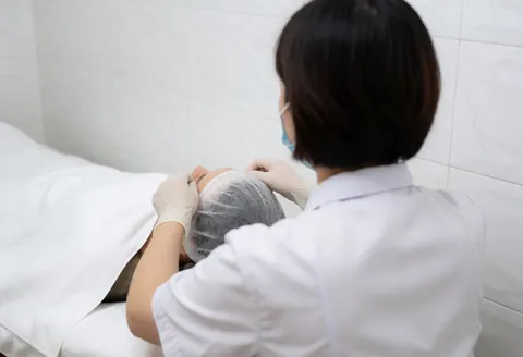 Dermatologist adjusting a cooling hood on a client resting on a treatment table in a clinical setting